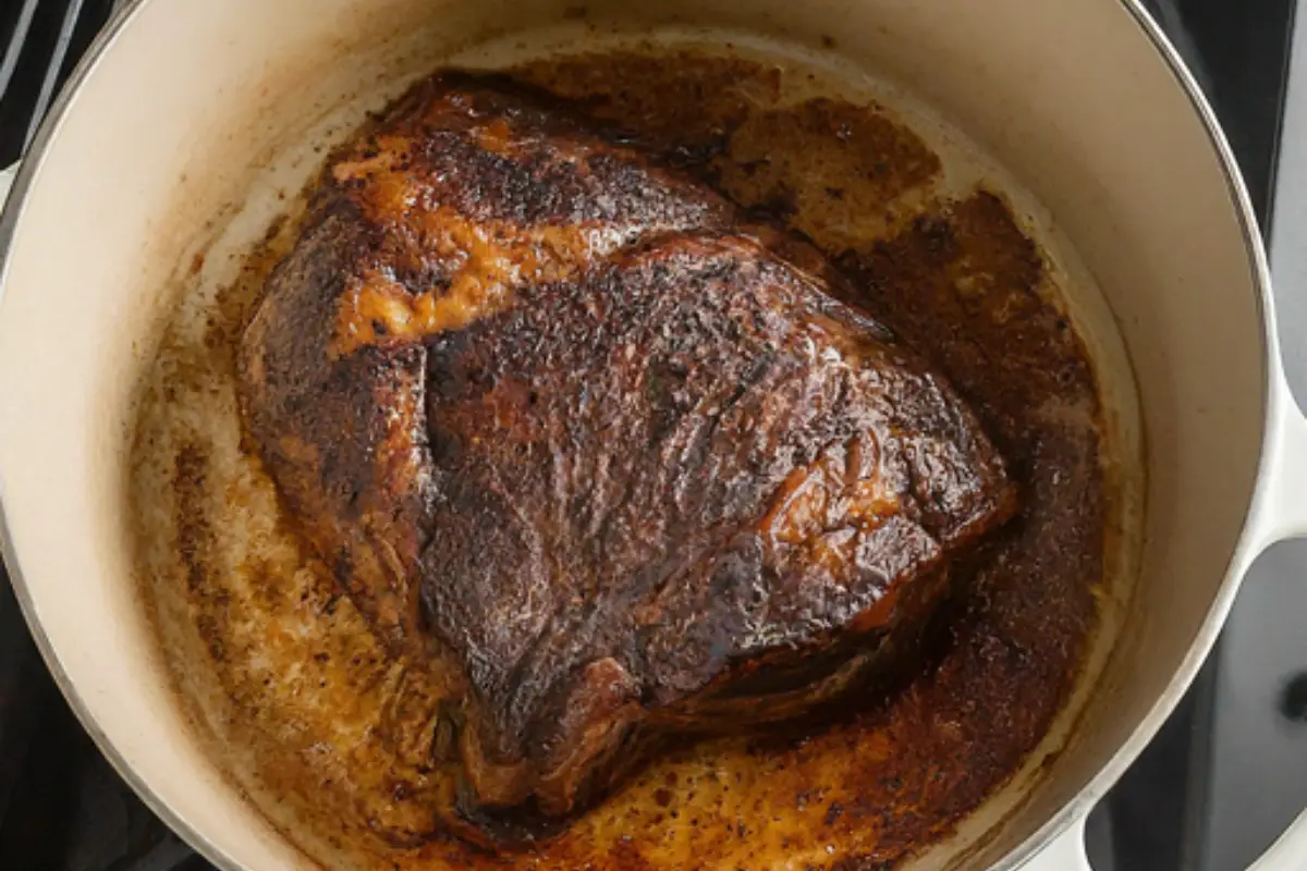 A juicy chuck roast with a deep golden brown sear sizzling in a hot Dutch oven on a stovetop. 