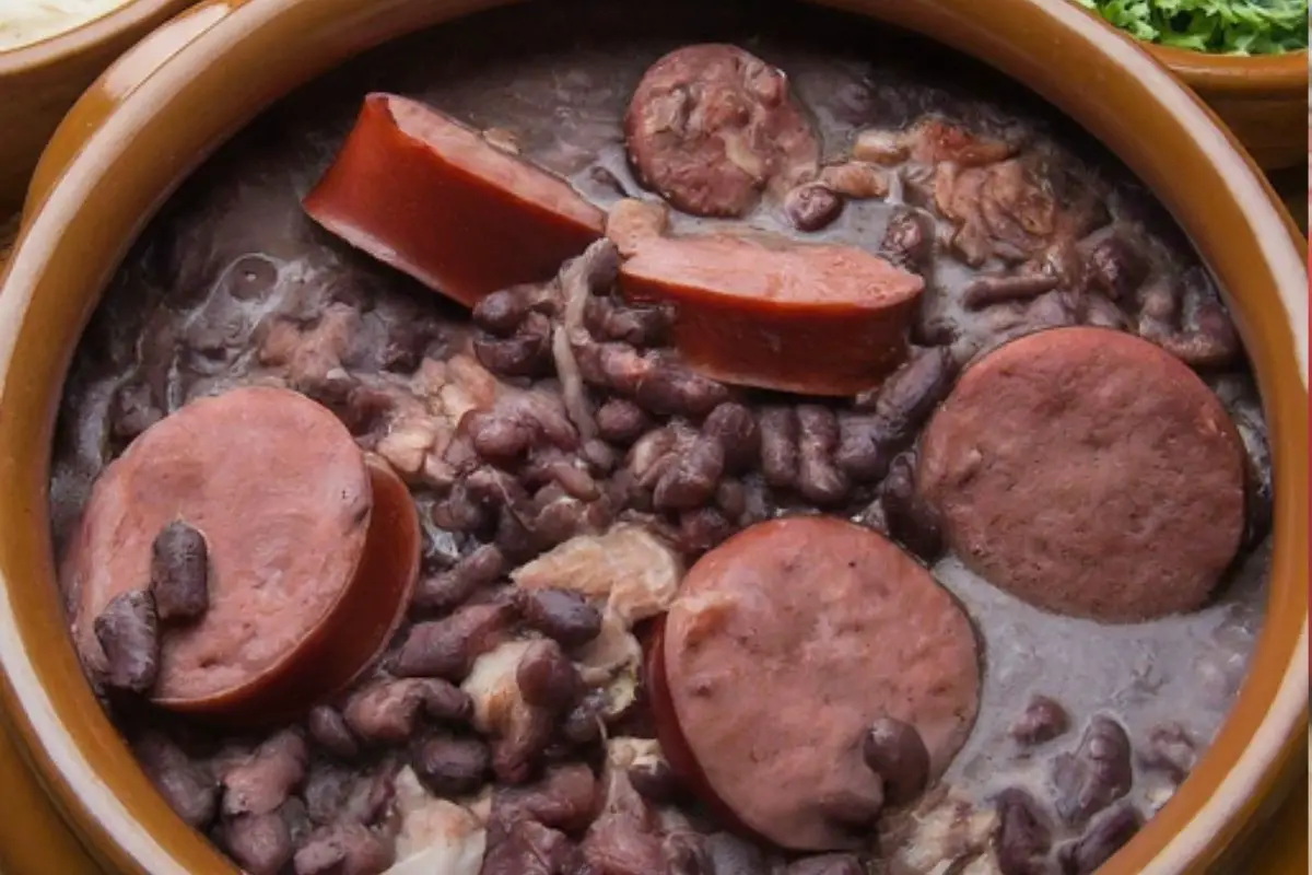 A close-up of a steaming bowl of Brazilian feijoada, a black bean stew with meats, vegetables, and aromatic spices